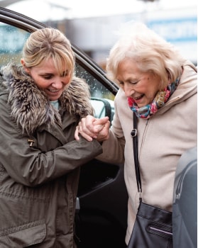 Younger woman assisting elder woman out of a vehicle