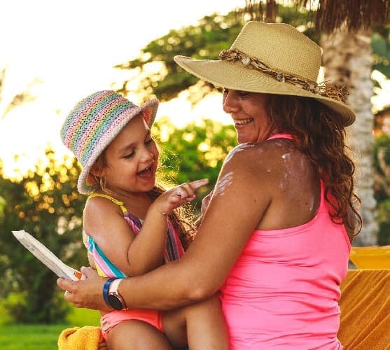Photo of a mother and daughter wearing bathing suits and hats and applying sunscreen