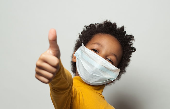 Happy African American child in medical protective face mask showing thumb up