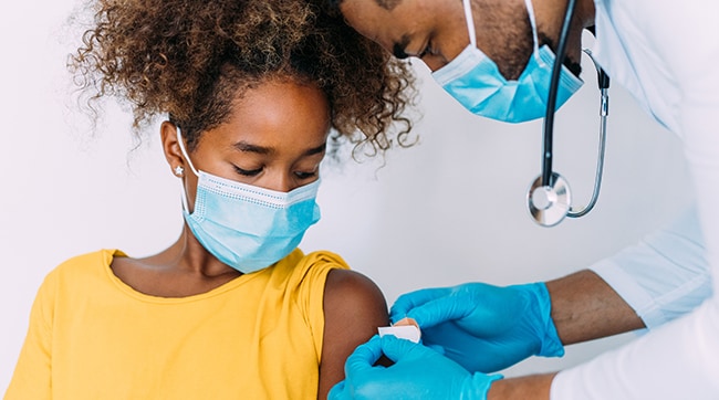 Un médico coloca un vendaje en el brazo de una niña después de recibir la vacuna