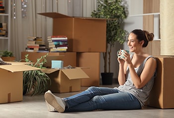Young woman sitting in her apartment among moving boxes