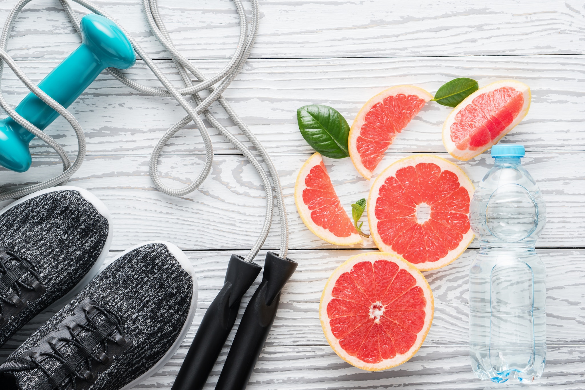 Sport shoes, rope, bottle of water and fresh grapefruits on rustic white wooden table, fitness accessories.