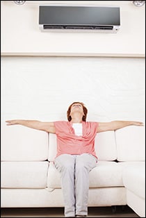 A woman sitting on a couch under an air conditioner, enjoying the cool breeze