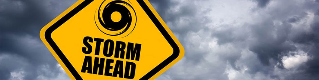 A yellow road sign with dark clouds behind it and an icon of a hurricane and words "Storm Ahead" signifying caution