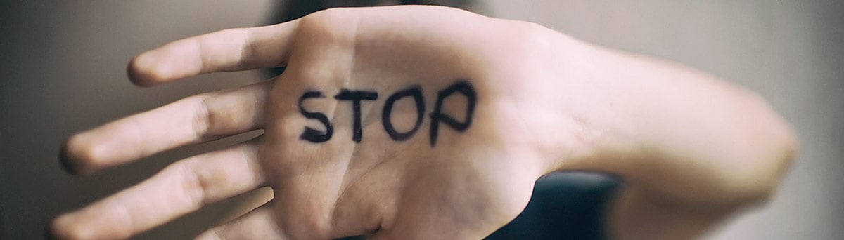 A young man’s covers his face with his hand, the word “stop” spelled out in black letters on his palm.