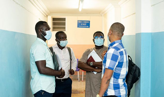 A group of four men that are stand in a hallway in conversation at a hospital in Ghana, 2021.