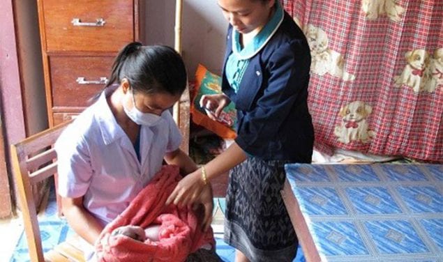 Woman holds newborn receiving a birth dose vaccination by a healthcare worker at a health facility in Lao.