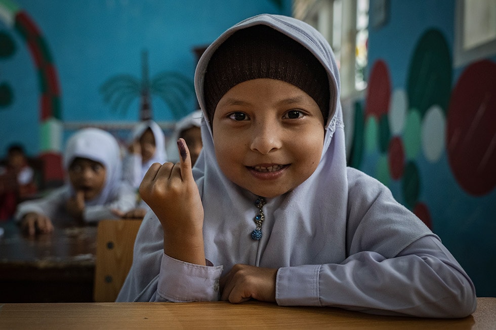 A child at school in Indonesia shows a mark on her finger that shows she has received an oral polio vaccine.
