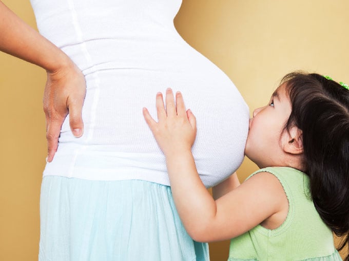 child kissing pregnant mother