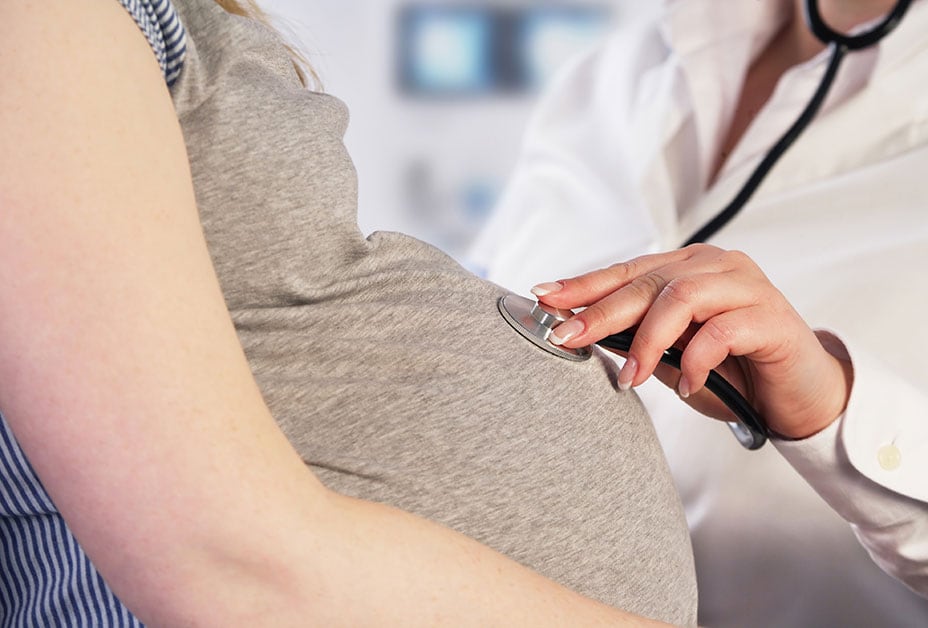 Doctor placing stethoscope on pregnant woman's belly