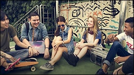 The figure shows a group of teenaged students sitting on the ground outdoors.