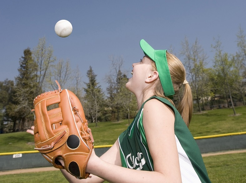 Female baseball player with a baseball mit throwing a ball in the air.
