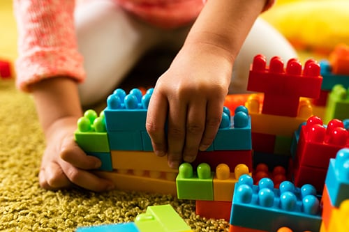 Close-up of child playing with toy blocks on the carpet.