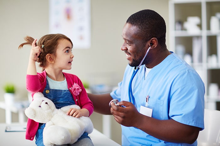 Little girl holding a teddy bear, talking to a doctor