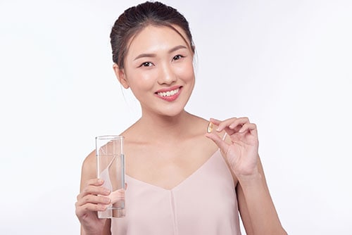 Smiling asian female model holding transparent glass in her hand.