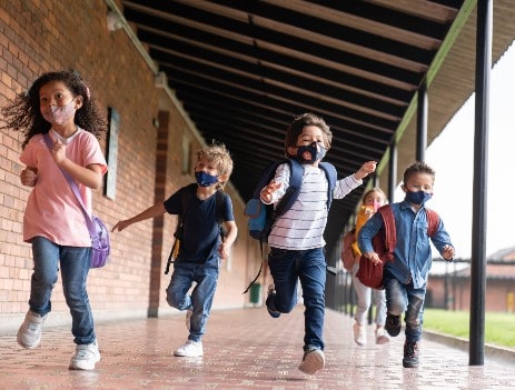 Children wearing protective face masks running down the hall
