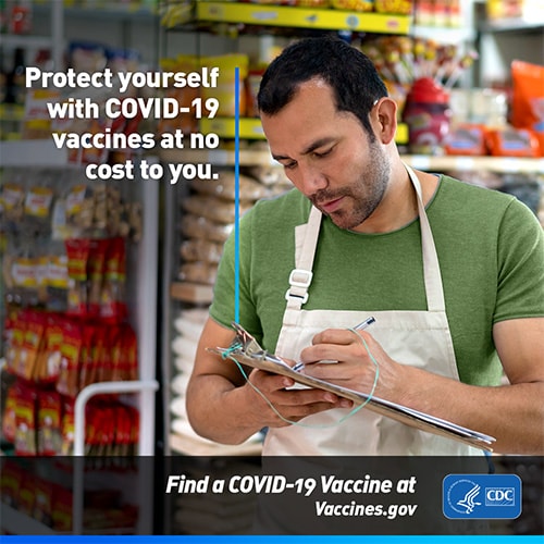 A grocery store employee completing paperwork. Text reads, 'Protect yourself with COVID-19 vaccines at no cost to you. Find a COVID-19 vaccine at vaccines.gov'