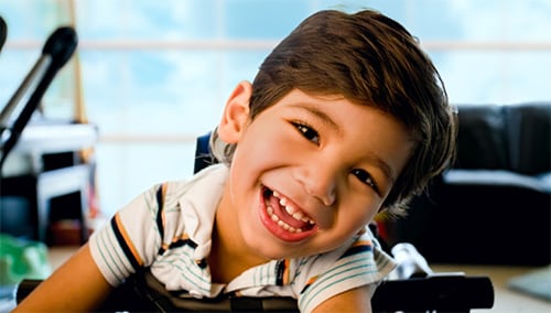 A young boy with cerebral palsy sitting in a chair and smiling.