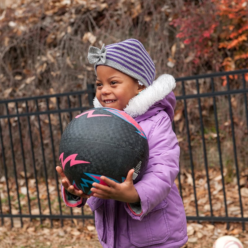 A young girl catches a ball outside on the playground.