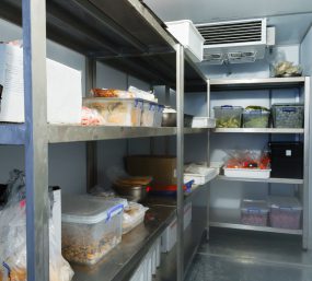 Large walk in refrigerator with steel shelves in a restaurant.