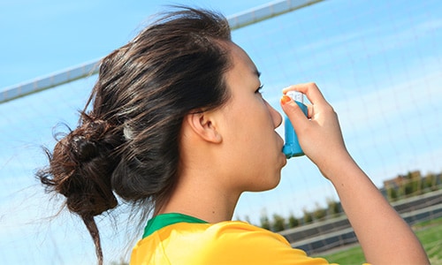 Young girl using asthma inhaler outdoors