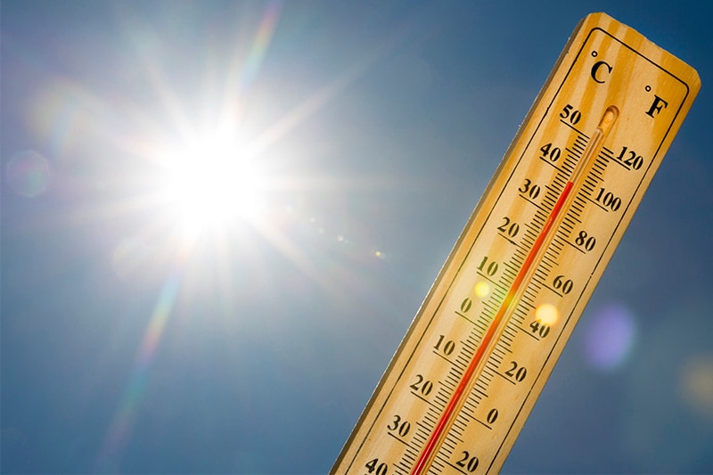 A thermometer marking 100 degrees Fahrenheit against a blue sunny sky.