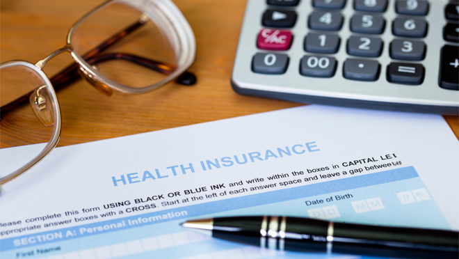 A form reading Health Insurance is on a table with a pen, calculator, and glasses