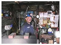 Seventy year old miner surrounded by tables of equipment inside a mine.