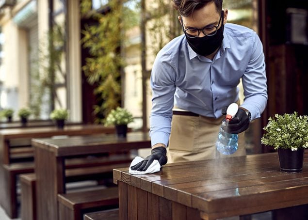 Man wiping down tables outside of restaurant