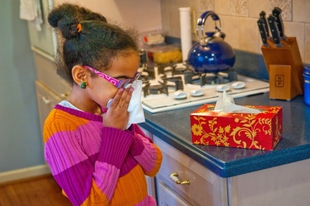 Little girl bloweing her nose with a tissue at home