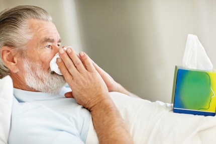 Older man blowing his nose while in bed sick