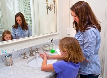 Mother helping her daughter wash her hands in bathroom sink.