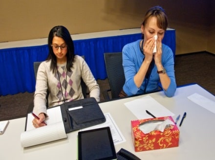 Woman covering her cough with a tissue while sitting beside a co-worker.