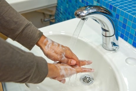 Woman washing her hands with soap and water in a sink at work.