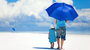 adult and child walking under blue umbrella at the beach