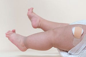 baby boy legs with a band-aid patch after taking a vaccine