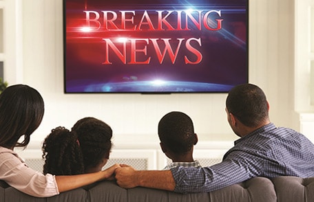 Una familia viendo la televisión. La pantalla del televisor dice "Noticias de última hora.