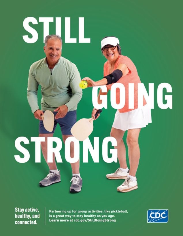 An older man and woman, wearing athletic clothing, are holding pickleball paddles and the woman is about to serve the ball.