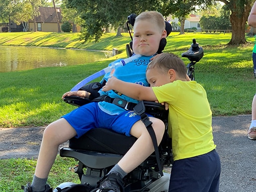 Jack sitting in his wheelchair as his brother gives him a hug.