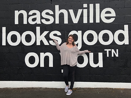 Sarah standing in front of a wall painting, 'nashville looks good on you'