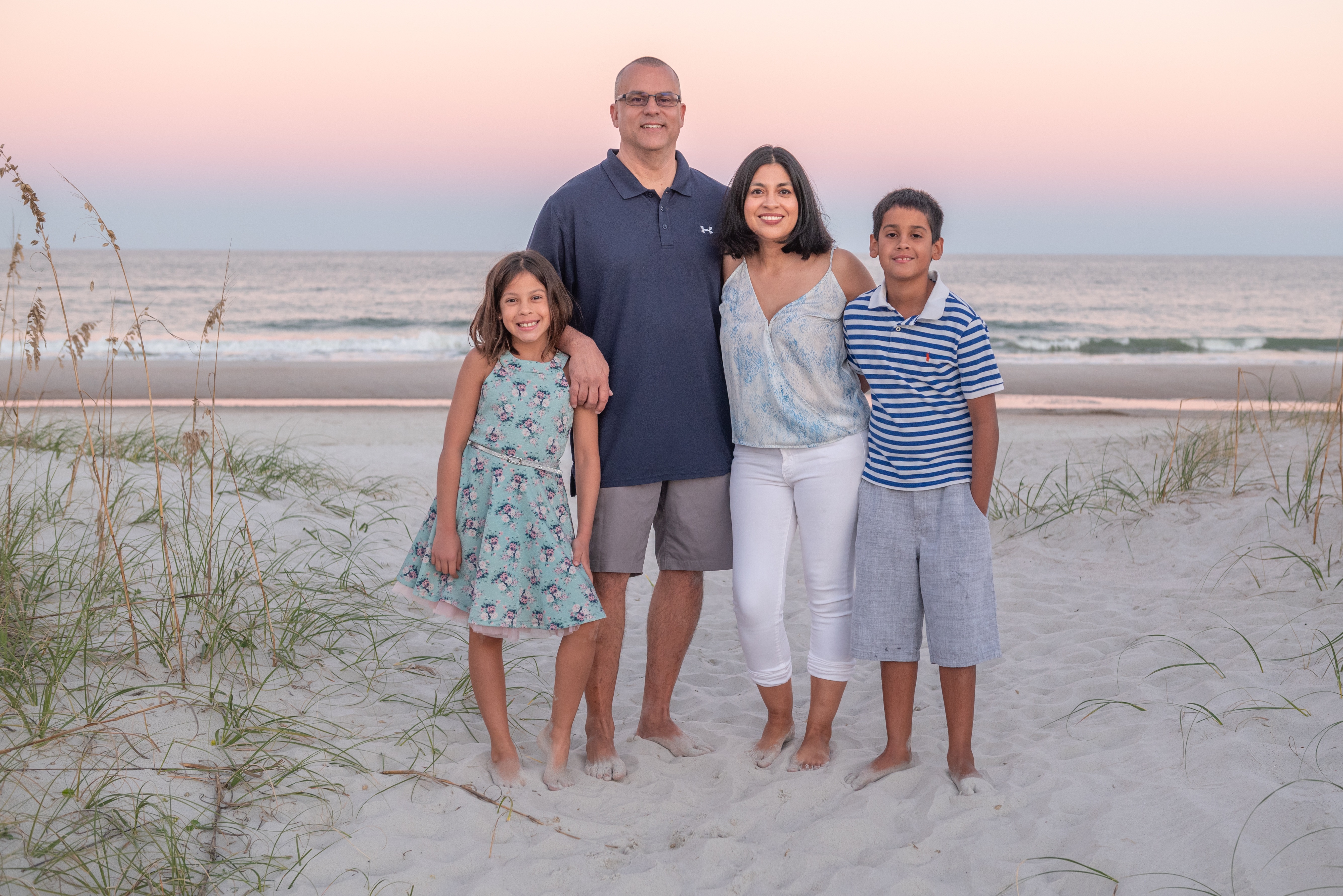 Nadia with her husband and two children standing together on a beach at sunset.