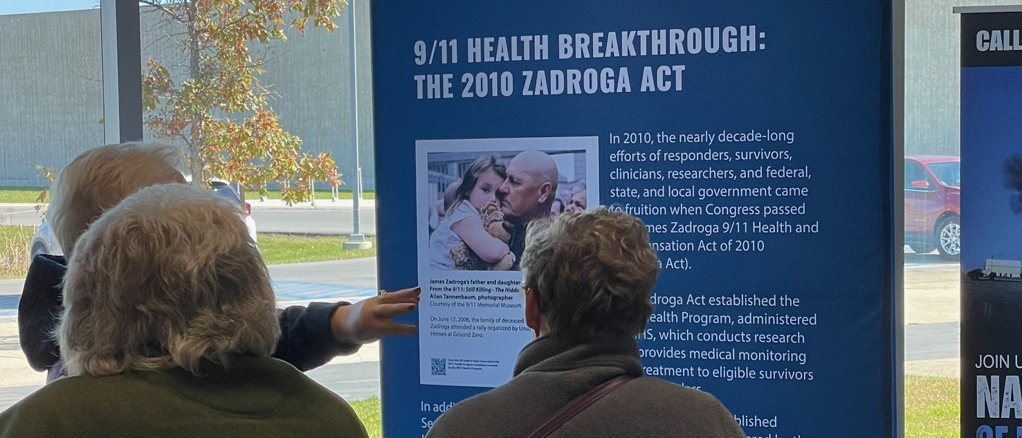 Visitor reading display panel titled ‘9/11 Health Breakthrough: The 2010 Zadroga Act.’ 
