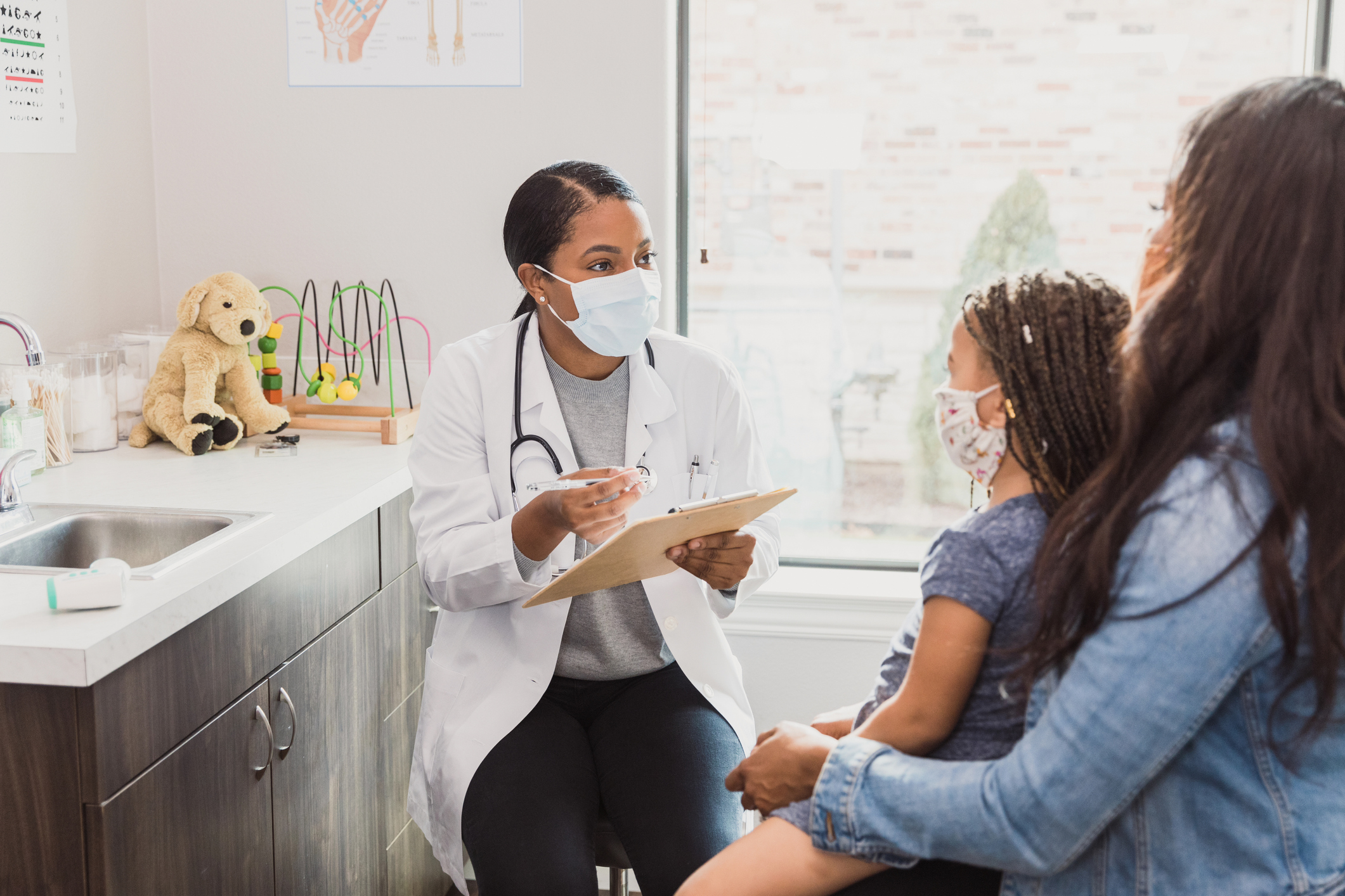 A mother and daughter sit in a doctor's office talking with a doctor.