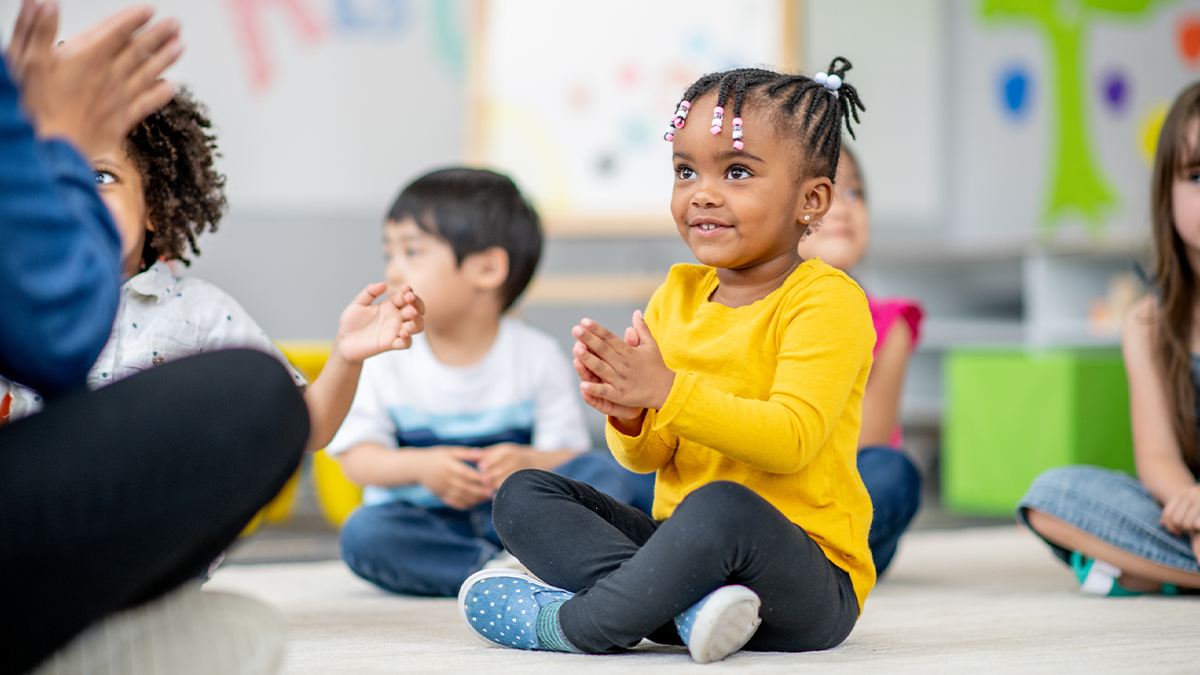 2 year old child sitting in a classroom and clapping hands.
