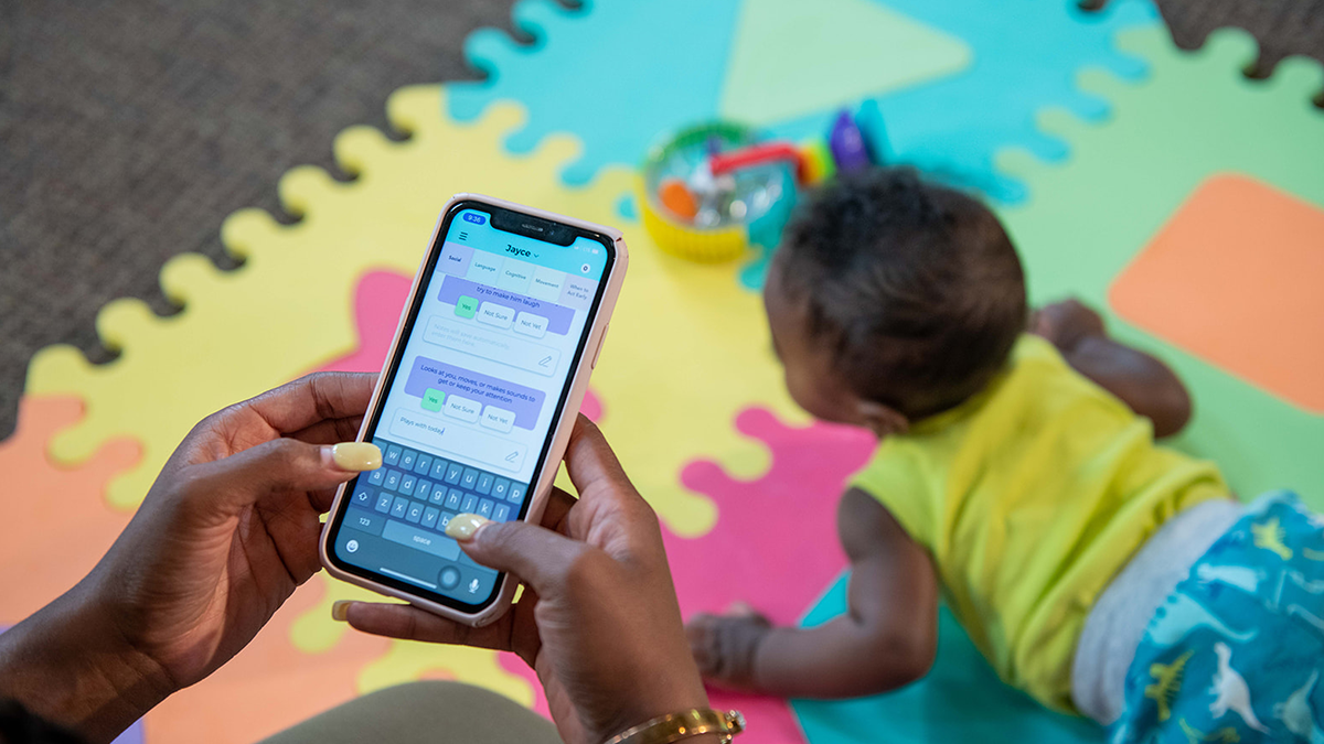 Mom using milestone tracker app next to baby
