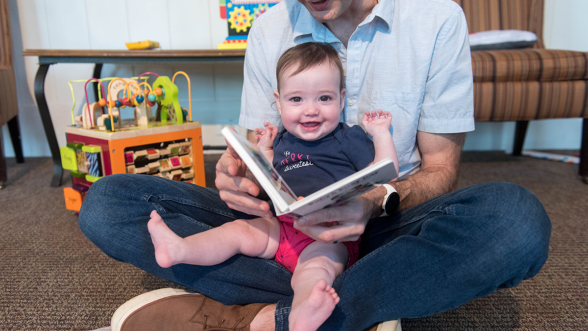 Dad reads a book to toddler in his lap.