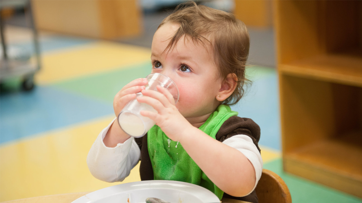 Child drinks from a cup using two hands to hold it