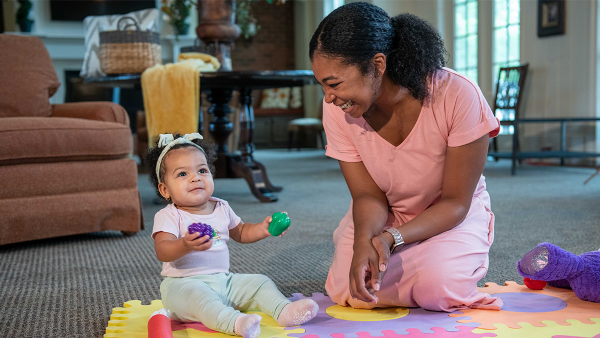 Baby sits with her mother and holds two toys in her hands