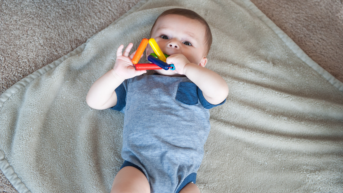 Baby puts a toy in his mouth laying on a blanket.