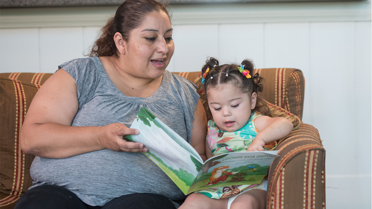 Mother and daughter read book sitting on the couch.
